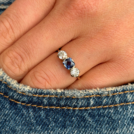 Antique, Edwardian sapphire and diamond three-stone engagement ring worn on hand.