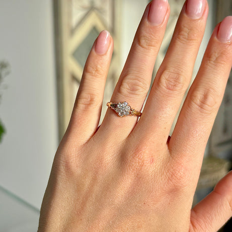 2093-Antique, Edwardian diamond daisy cluster ring held in fingers