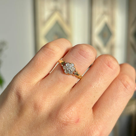 2093-Antique, Edwardian diamond daisy cluster ring held in fingers worn on hand.