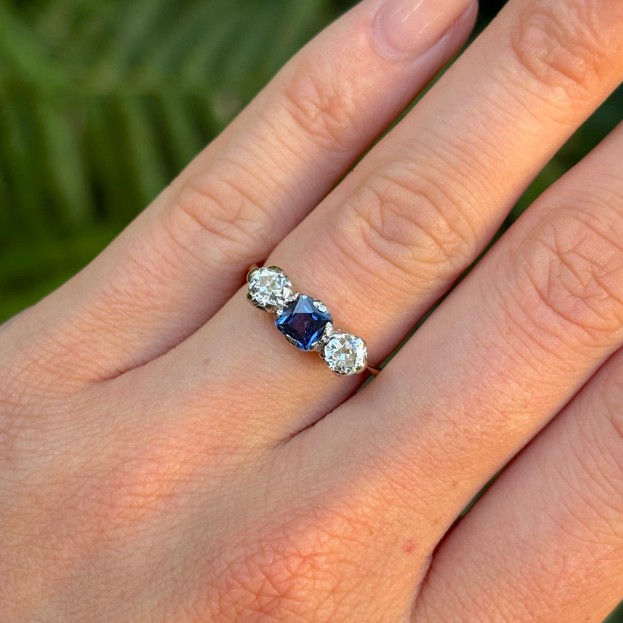 Antique, Edwardian sapphire and diamond three-stone engagement ring worn on hand.