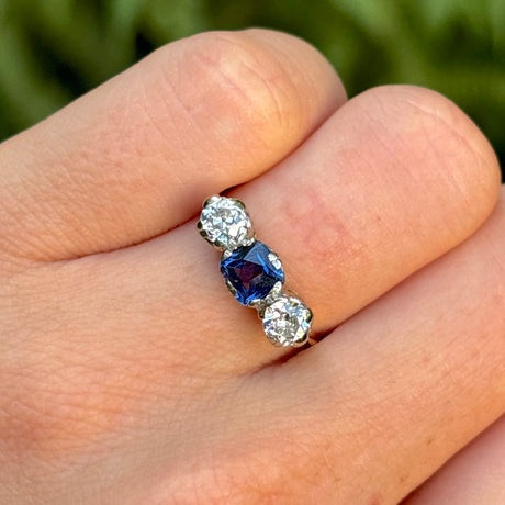 Antique, Edwardian sapphire and diamond three-stone engagement ring worn on hand.