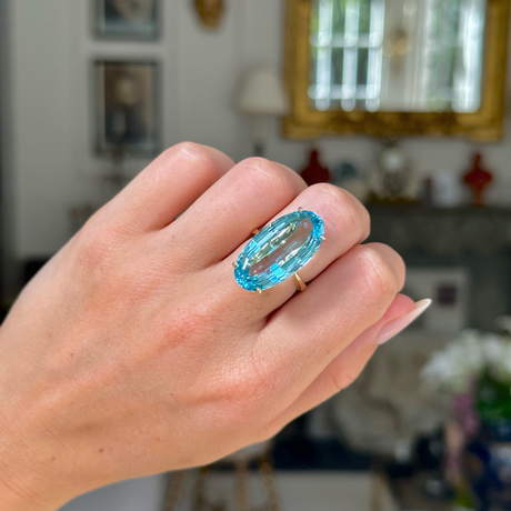 aquamarine and yellow gold cocktail ring on left hand, middle finger. Photographed with hand held in fist and antiquated bokeh background. 