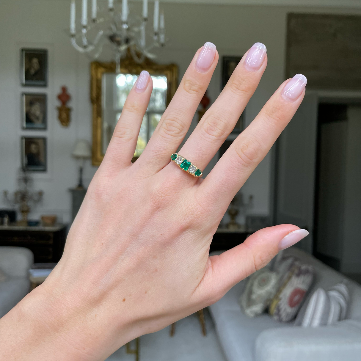 Five stone emerald and diamond ring worn on hand.