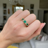 Five stone emerald and diamond ring worn on closed hand.