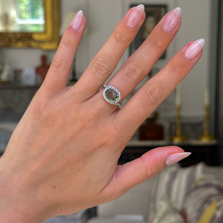 Green sapphire and diamond ring worn on left middle finger, hand in frame and bokeh antiquated background