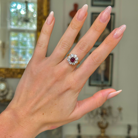 antique ruby and diamond cluster ring worn on the middle finger on a hand, shot with an antiquated bokeh background