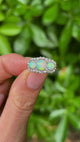 Antique, Victorian three-stone opal & diamond cluster ring held in fingers.