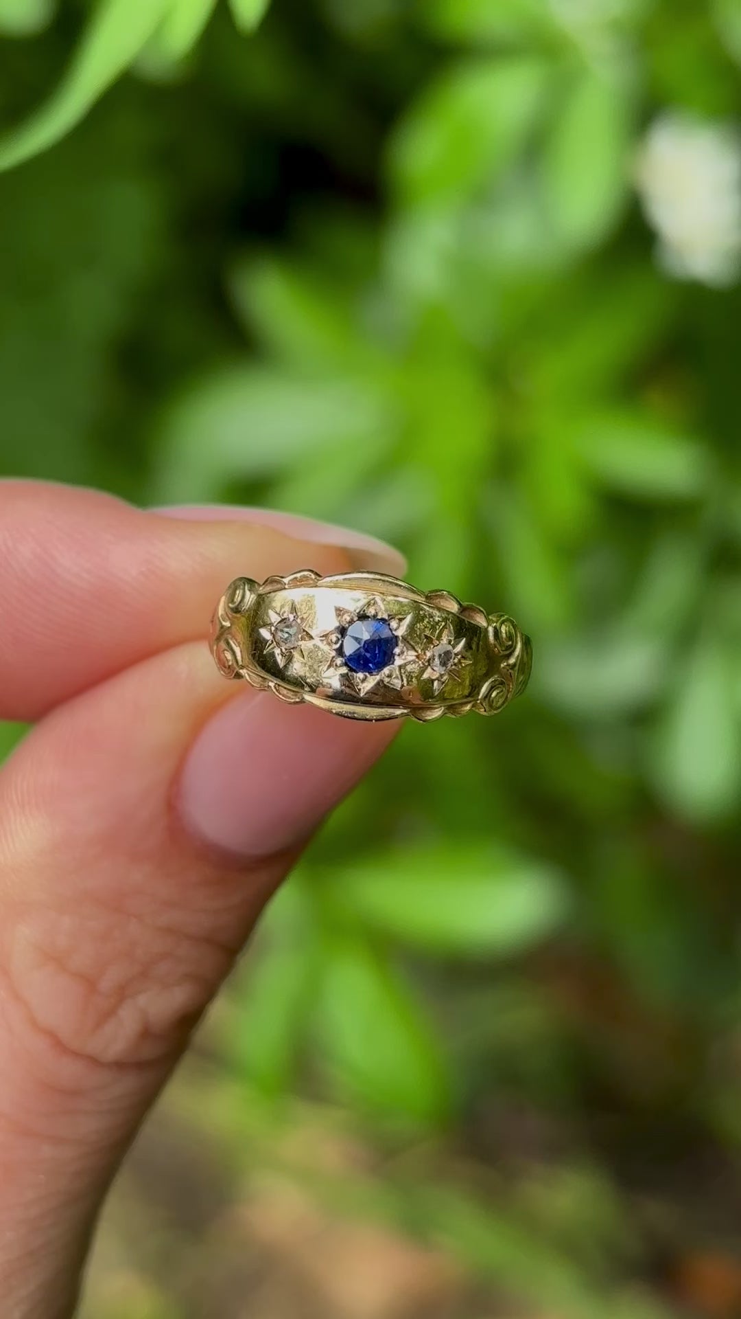 Antique, Edwardian sapphire and diamond three-stone gypsy ring held in fingers.