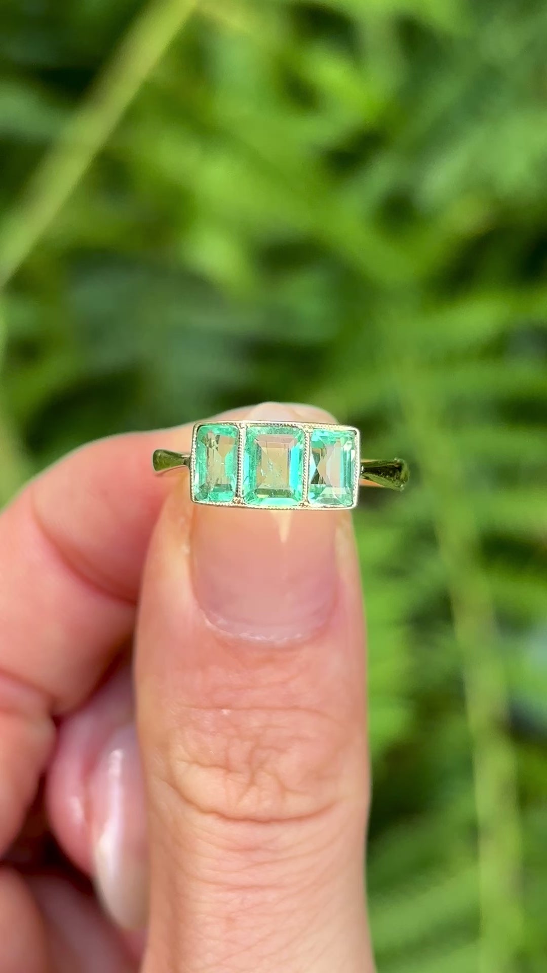 Vintage, 1930s three-stone emerald ring held in fingers. 