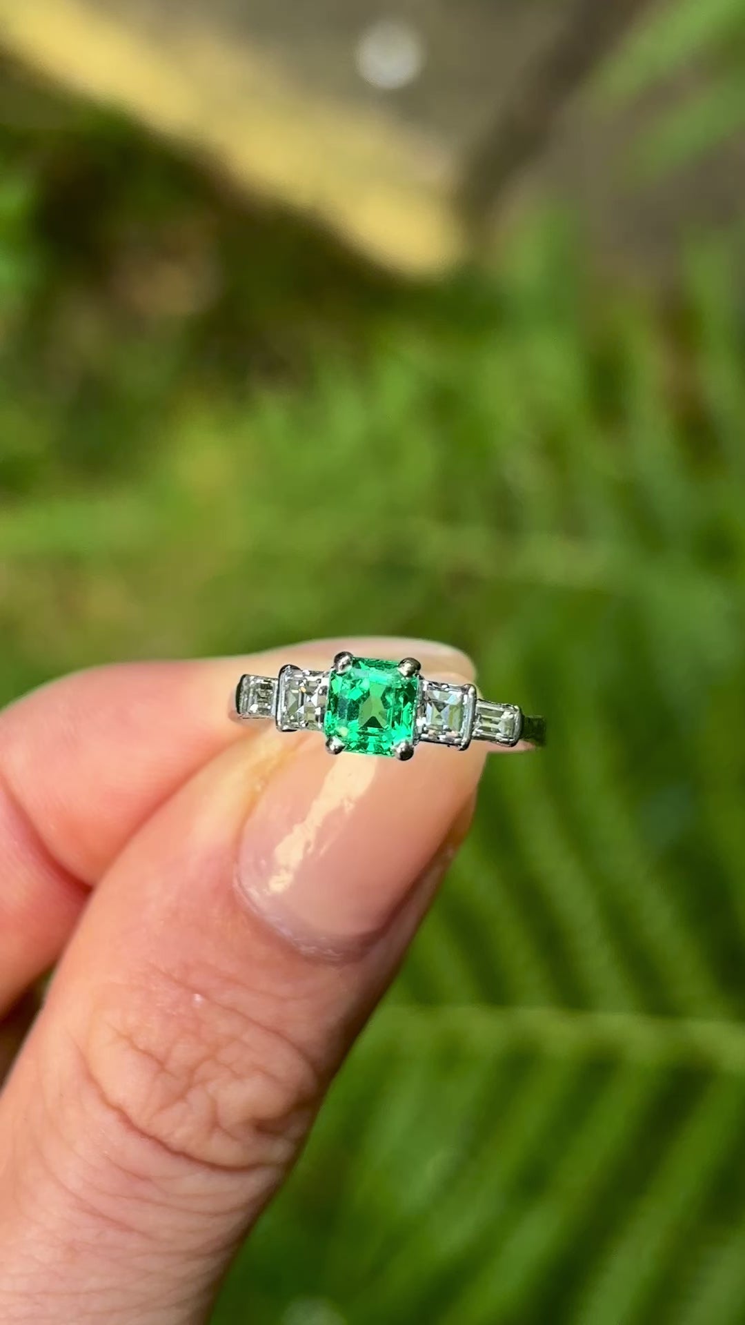 Vintage, Art Deco emerald & diamond five-stone ring held in fingers.