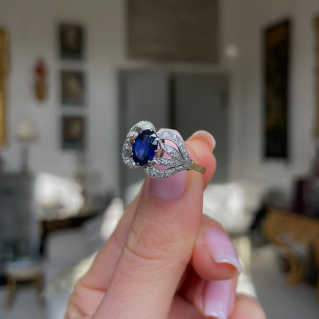 Art Nouveau, sapphire and diamond ring, held in fingers.