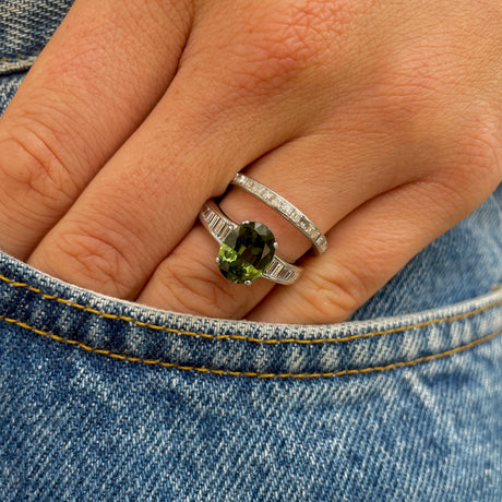 Green sapphire and diamond engagement ring worn on hand in pocket of denim jeans. 