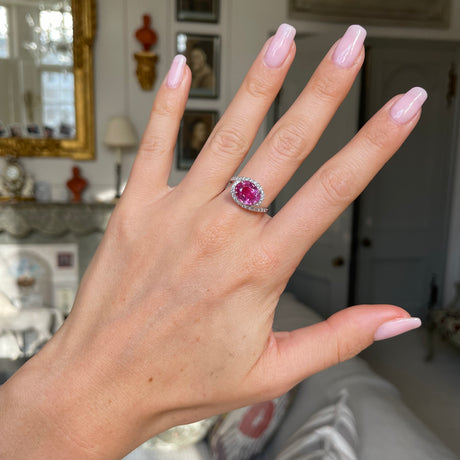 Pink sapphire and diamond engagement ring, worn on hand.